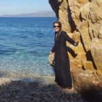 Thedi, founder of Path Travel Designs standing by a large rock at a beach in Greece - 10 reasons to book with me