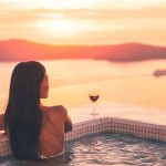 A woman looking out to the view of the Santorini from the private pool with a glass of wine, a truly romantic destination
