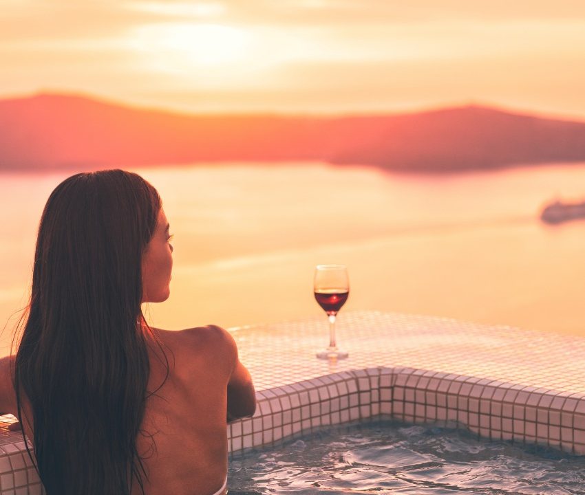 A woman looking out to the view of the Santorini from the private pool with a glass of wine, a truly romantic destination