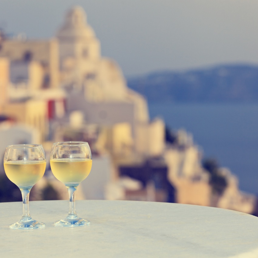 Two wine glasses with Santorini buildings as the backdrop, part of a private wine tasting tour in this romantic destination